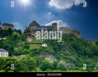 Die Reichsburg Cochem, eine mittelalterliche Burg, steht majestätisch auf einem Hügel, umgeben von üppiger grüner Vegetation, unter einer hellen Sonne mit dramatischen Wolken i Stockfoto