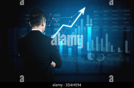 Ein Geschäftsmann steht zuversichtlich und analysiert digitale Diagramme und Diagramme, die das Finanzwachstum und die Trends darstellen, und hebt Datenanalysen in einer modernen Form hervor Stockfoto