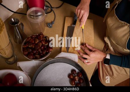 Eine Person hackt Kastanien auf einem hölzernen Schneidebrett in einer gemütlichen Küche, umgeben von Schüsseln mit Kastanien, einem Mixer und Utensilien, und fängt einen Krieg ein Stockfoto