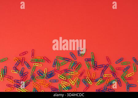 Bunte Büroklammern auf rotem Hintergrund. Bürobedarf und Kreativkonzept. Büroklammern für Schul- und Bastelprojekte. Stockfoto