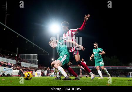 Scott Robertson von Notts County (links) und Jonathan Tomkinson von Cheltenham Town (Mitte) kämpfen um den Ball während des Spiels der Sky Bet League Two im EV Charger Points Stadium in Cheltenham 2025. Stockfoto