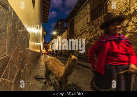 Nächtliche Szenen im historischen Viertel von Cusco, mit Einwohnern und Lama, die durch die beleuchteten Straßen der Inka-Steine im Viertel San Blas schlendern Stockfoto