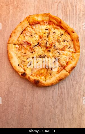 Blick von oben auf köstliche Pizza mit geschmolzenem Käse und Pilzen auf Holztisch, warme Farben und knusprige Kruste Stockfoto