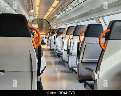 Modernes Zuginnere mit leeren Sitzen und orangefarbenen Griffen, sauberes Design des öffentlichen Nahverkehrs, komfortables Reisekonzept für Fahrgäste Stockfoto
