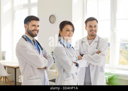 Porträt glücklicher selbstbewusster junger Ärzte, die mit gekreuzten Armen im Krankenhaus oder in der medizinischen Klinik stehen. Stockfoto