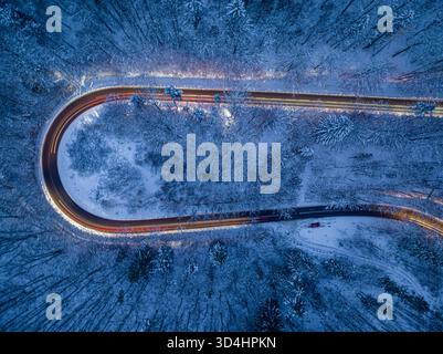 Autoscheinwerfer beleuchten eine kurvenreiche Winterstraße und verschneite Vorder. Transport im Winter bei Nacht. Stockfoto