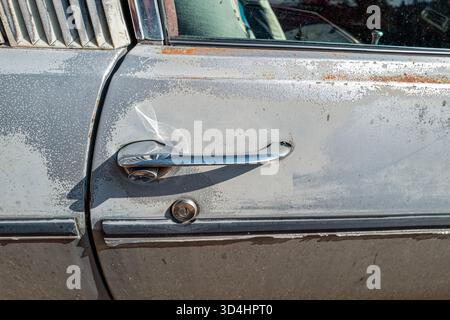 Das Detail des Schlosses und des Türgriffs auf der Beifahrerseite eines verblassten weißen Autos Stockfoto