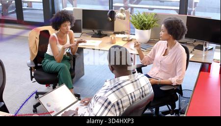 Besprechung von drei Kollegen im Business Casual Gesten im Großraumbüro mit Laptop-Chart Stockfoto