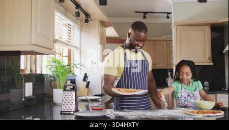 Gekochte Pizza halten, Eltern und Kind streuen Mehl auf den Teig, tragen Schürzen Stockfoto