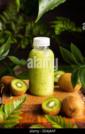 Ein erfrischender Kiwi-Smoothie befindet sich in einer klaren Flasche, umgeben von ganzen Kiwis und Fuzzy Kiwis. Grüne Blätter verleihen dem natürlichen setti einen lebendigen Touch Stockfoto