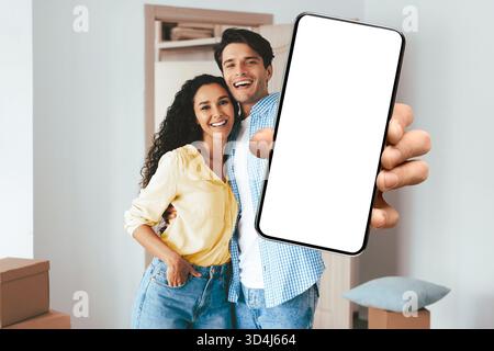 Ein Paar lächelt und hält ein Smartphone in einem hellen Wohnraum Stockfoto