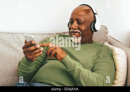 Ein Senior Mann genießt Musik, während er sich am Nachmittag auf einer Couch zu Hause entspannt Stockfoto