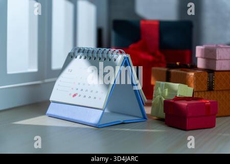 Ein Dezember-Schreibtischkalender, der Weihnachten und den zweiten Weihnachtsfeiertag hervorhebt, ist umgeben von farbenfrohen Geschenkboxen in verschiedenen Größen, die Weihnachtsverkäufe symbolisieren Stockfoto