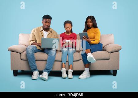 Familie entspannt sich gemeinsam auf einem Sofa, während elektronische Geräte in einer hellen Umgebung verwendet werden Stockfoto