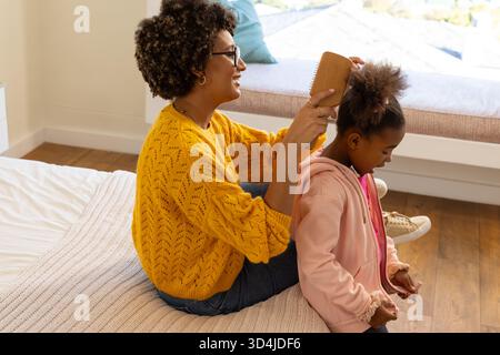 Haare putzen, Mutter und Tochter im Schlafzimmer sitzen auf dem Bett, mit Holzhaarbürste Stockfoto