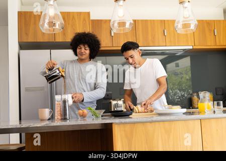Kochen Frühstück verschiedene männliche Freunde schneiden Brot und gießen Kaffee in der Küche, mit Saft Stockfoto