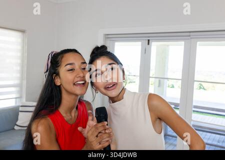 Singen Sie verschiedene weibliche Freunde mit Mikrofon in einem hellen Wohnzimmer mit gestreiften Kissen Stockfoto Singen Sie verschiedene weibliche Freunde mit Mikrofon in einem hellen Wohnzimmer mit gestreiften Kissen Stockfoto