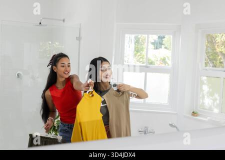 In gelben und beigefarbenen Kleidern bewundert das Bad mit Spiegel verschiedene weibliche Freunde Stockfoto