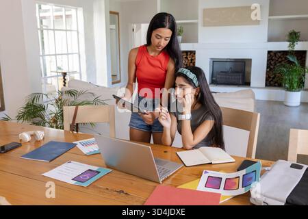 Zusammenarbeit mit Freundinnen, die im Wohnzimmer auf einem Laptop oder Tablet skizzieren, mit Farbmustern Stockfoto