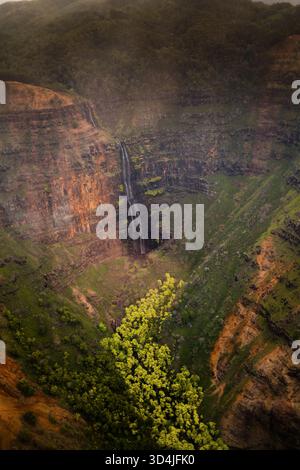 Ein vertikales Luftbild von Waipoo Falls, einem hohen Wasserfall, der die roten und grünen Klippen des Waimea Canyon in Kauai, Hawaii, herabstürzt. Stockfoto