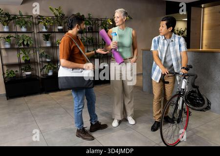 In der modernen Lobby mit Yogamatte und Fahrrad unterhalten sich verschiedene Freunde Stockfoto