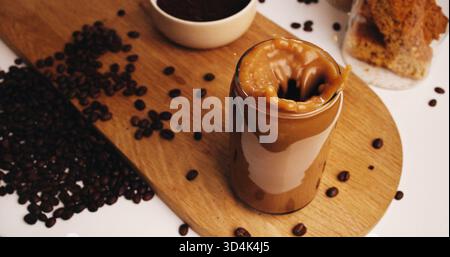 Spritzer, Kaffee und Bohnen mit Glas auf dem Tisch in der Küche zu Hause für Koffein-Getränk, Frühstück und morgendliches Brauen. Cappuccino, Eis Latte Drink und Stockfoto