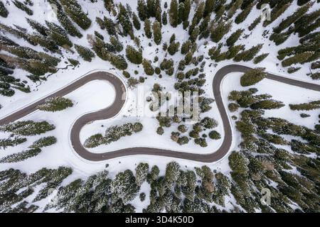 Aus der Vogelperspektive sehen Sie eine gewundene Straße, die durch schneebedeckte immergrüne schneidet, den Asphalt, ein dunkles Band vor der weißen Umarmung des Winters, Passo Giau, The Do Stockfoto