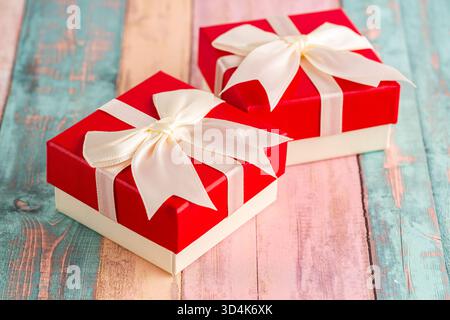 Zwei Geschenkboxen mit Bändern auf buntem Holzhintergrund. Weiße und rote Geschenkschachteln mit weißen Bändern in Nahaufnahme. Stockfoto
