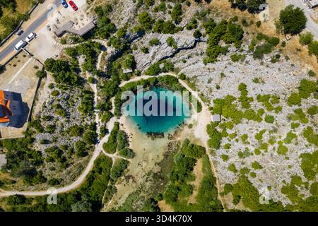 Blick aus der Vogelperspektive auf das Drachenauge, eine tiefblaue Karstquelle, umgeben von schroffen weißen Felsen und üppiger grüner Vegetation, Cetina, Kroatien. Stockfoto