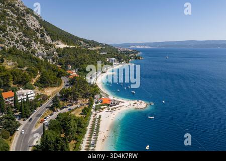 Aus der Vogelperspektive auf die türkisfarbene Adria, die den Sandstrand küsst, eingebettet zwischen der Küstenstraße und der zerklüfteten Bergkulisse, Omis, Split-Dalmatien Stockfoto