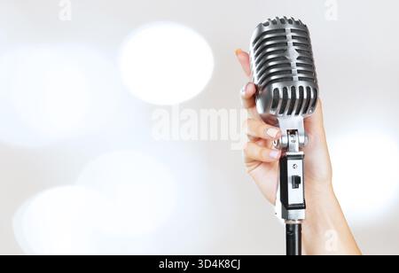 Frauenhand hält ein Vintage-Mikrofon auf hellem Hintergrund Stockfoto