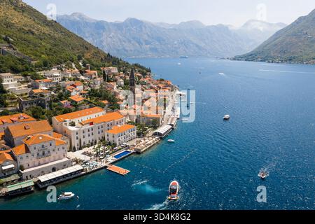 Blick aus der Vogelperspektive auf die Terrakotta-Dächer, die hinunterstürzen und auf das azurblaue Wasser rund um die historische Kirche St. Nikolaus, Perast, Gemeinde Kotor treffen Stockfoto