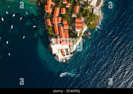 Aus der Vogelperspektive treffen die Terrakotta-Dächer auf das türkisfarbene Meer und verbinden künstliche Strukturen mit der natürlichen Schönheit der Küste, Sveti Stefan, Budva Stockfoto