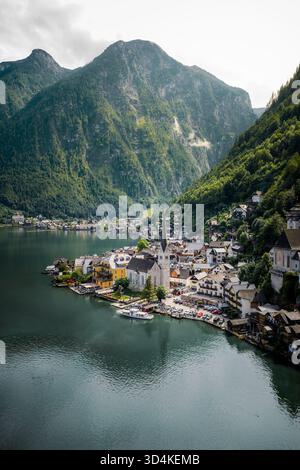 Aus der Vogelperspektive auf den ruhigen See, der die majestätischen Berge widerspiegelt, liegt das Dorf Hallstatt am Ufer mit seinem berühmten Kirchturm, der in die Tiefe dringt Stockfoto