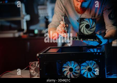 Ein Mann benutzt einen elektrischen Schraubendreher, um einen Desktop-Computer zu aktualisieren und zu reparieren. Konzept der modernen Technologie, Wartung, Heimwerkerreparatur und Computerhardware Stockfoto