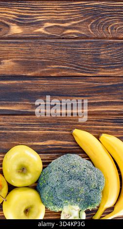 Ein Blick von oben auf frischen Brokkoli, Bananen und in Scheiben geschnittene Äpfel auf einer rustikalen Holzoberfläche. Stockfoto