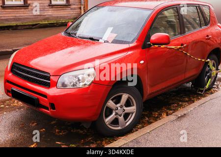 Nahaufnahme eines roten Hinterrads mit einer gelb-schwarzen Radklemme (Kofferraum) für eine Parklücke an einer Herbstkante. Hochwertige Fotos Stockfoto
