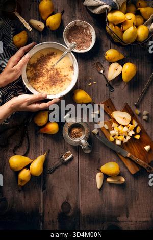 Flacher Zubereitungsprozess eines Birnenkuchens, Teig in einer Schüssel mit Kakao, Zucker und einem Schneidebrett, in dem Birnenkuchen in kleine Stücke geschnitten ist, hält jemand das Stockfoto