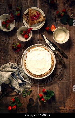 Frische Erdbeeren und Crepes Zubereitung mit Schlagsahne auf Holztisch Stockfoto