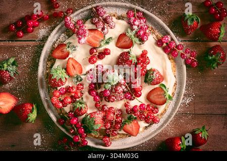 Hausgemachte Crepes auf Teller, dekoriert mit Schlagsahne, Puderzucker und einer Mischung aus Preiselbeeren und Erdbeeren, auf Holztisch Stockfoto