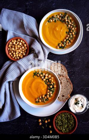 Saisonaler Kürbis, Süßkartoffel und Apfelsuppe. Schüsseln Suppe mit dekorativ gerösteten Kichererbsen, Kürbiskernen, Sauerrahm und gehackter Petersilie Stockfoto