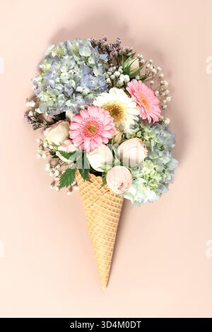 Kreatives Blumenarrangement mit Rosen, Hortensien und Gänseblümchen in Waffelkegel auf weichem, rotem Hintergrund. Stockfoto