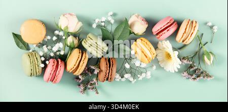 Farbenfrohe Macarons mit Rosen und Wildblumen auf einer weichen mintgrünen Oberfläche. Süße, blumige und vom Frühling inspirierte Ästhetik. Stockfoto