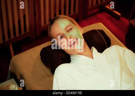 Die ruhige Atmosphäre des Spa-Salons, die lächelnde und verjüngende Kundin mit einer luxuriösen Gesichtscreme-Massage mit warmer Kerze. Gesichtshaut Stockfoto