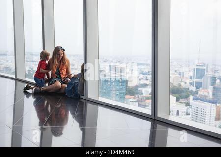 Frau, zwei Kinder sehen von der Aussichtsplattform des modernen Wolkenkratzers aus einen Panoramablick auf Ho Chi Minh City. Urbaner Lebensstil, reisen mit Kindern. Stockfoto
