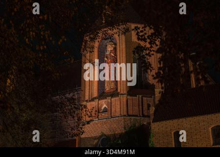 Nächtliche Nahaufnahme der Burg Malbork in Polen, mit beleuchteter roter Backsteinnische und hoher polychromer Madonna und Kind über Festungsmauern, Bögen und Stockfoto