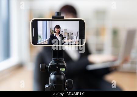 Kaukasische Frau in Geschäftskleidung, die sich auf dem Smartphone aufzeichnet und geschäftliche Themen im Büroumfeld diskutiert. Konzept des Video-Bloggens, online Stockfoto
