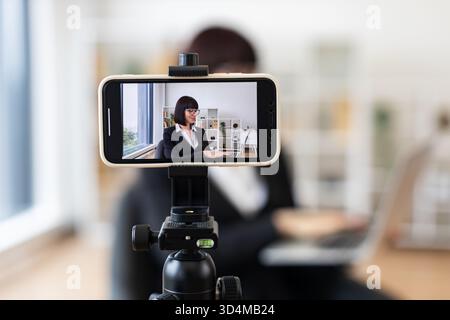 Kaukasische Frau in Geschäftskleidung, die sich auf dem Smartphone aufzeichnet und geschäftliche Themen im Büroumfeld diskutiert. Konzept des Video-Bloggens, online Stockfoto
