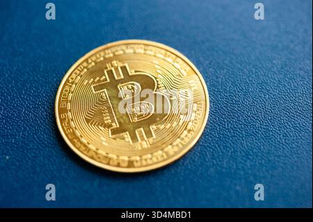 Gold Bitcoin physische Münze auf blauem texturiertem Hintergrund, die Kryptowährung und digitale Finanzen repräsentiert Stockfoto