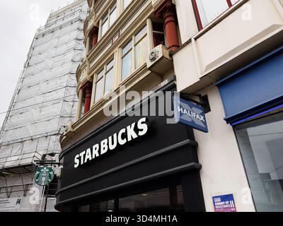Manchester, Großbritannien - 30. September 2025: Starbucks-Fassade in Manchester, Großbritannien, mit Halifax-Schild an einem historischen Gebäude und einer städtischen Ladenfront. Stockfoto